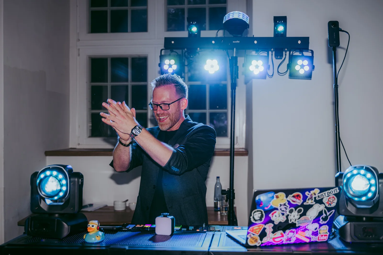 DJ Airbeck klatscht am Pult, vor Lichttechnik und Fenster