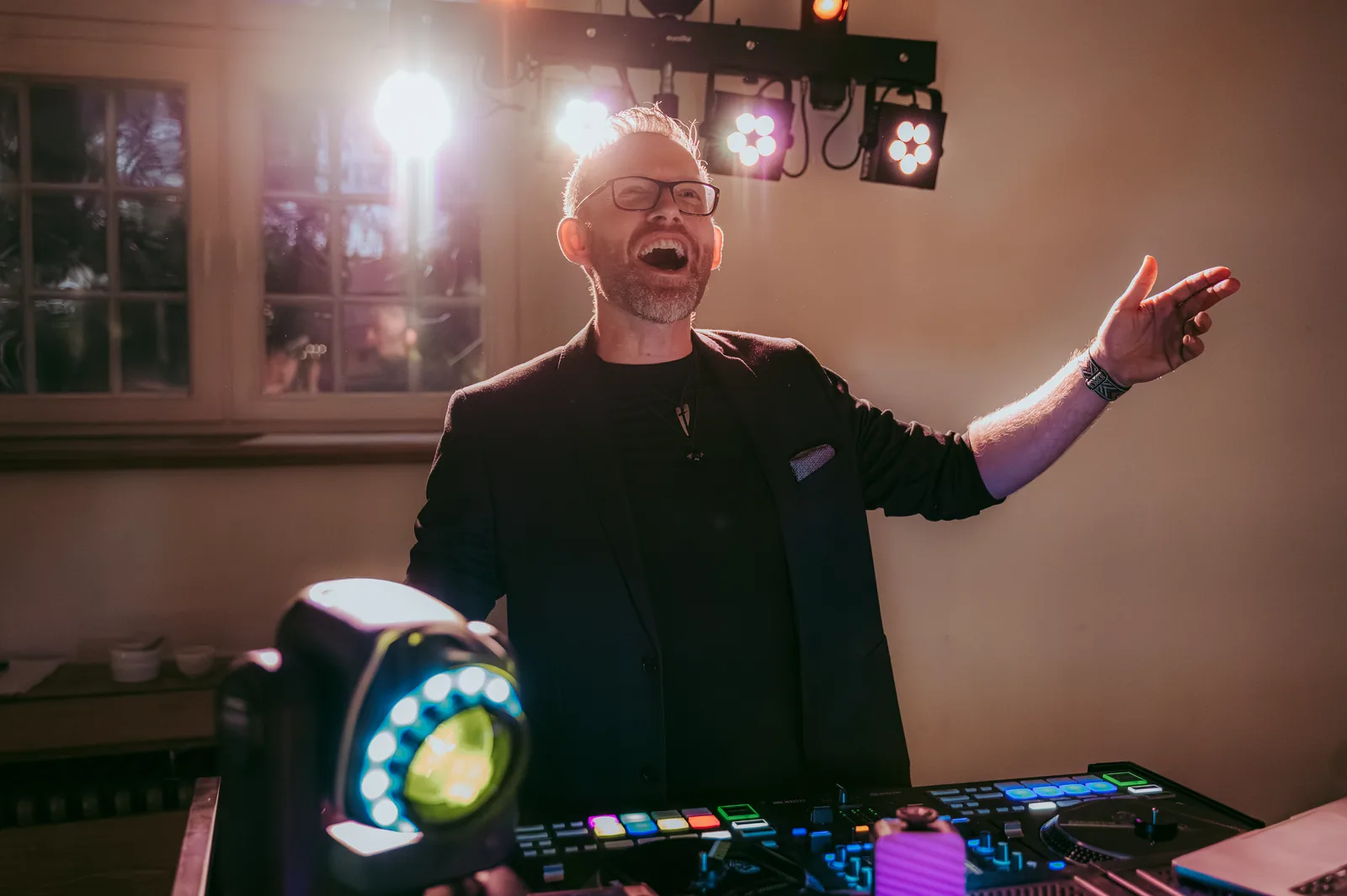 DJ Airbeck lacht und zeigt in den Raum, Moving Head im Vordergrund